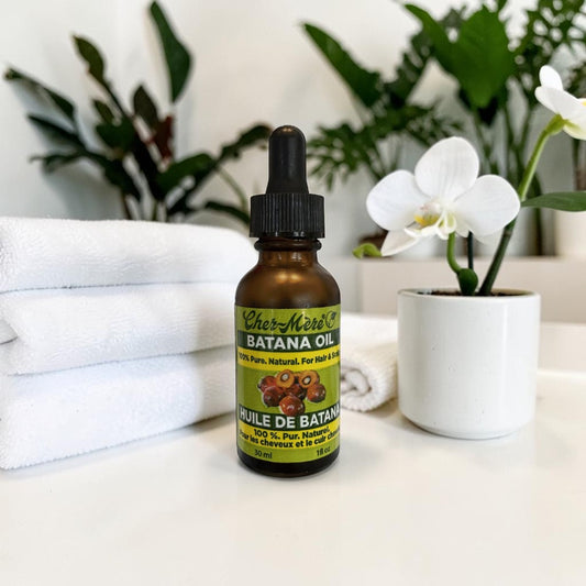 Bottle of Batana oil with a dropper on a surface with plants and towels in the background
