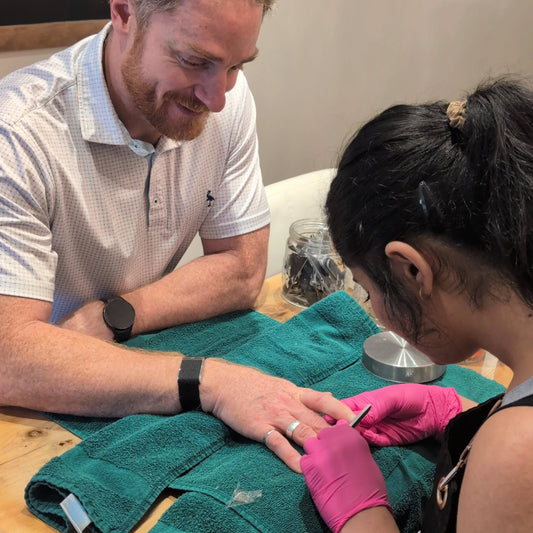 Father getting a manicure at a spa by a woman wearing pink gloves.